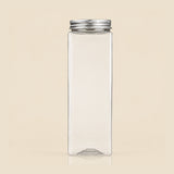 A clear rectangular glass bottle with a silver metal screw cap, centered on a solid beige background.