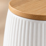 Close-up of a white ribbed ceramic container with a round natural bamboo lid, showing the wood grain texture and the ceramic ribbed surface.