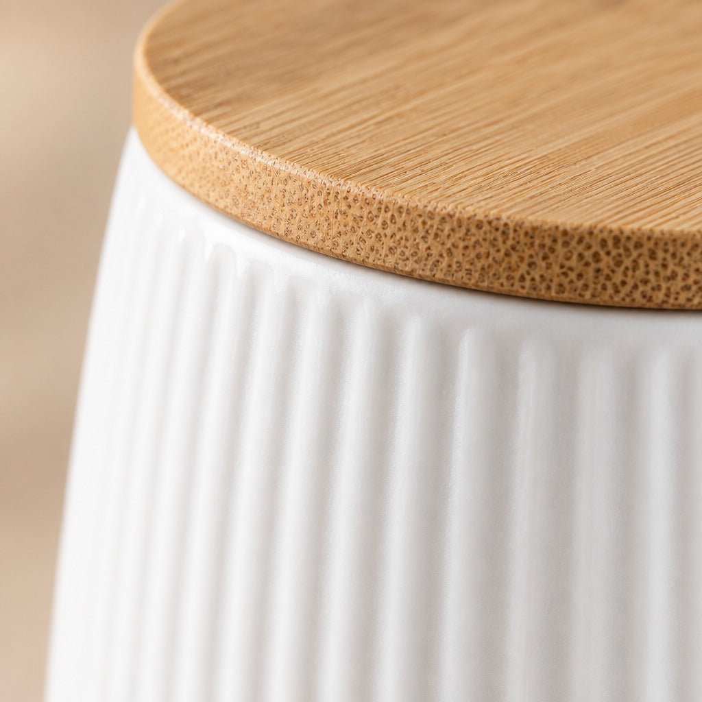 Close-up of a white ribbed ceramic container with a round natural bamboo lid, showing the wood grain texture and the ceramic ribbed surface.