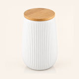 A white ribbed ceramic jar with a natural bamboo wood lid, shown on a light cream background.