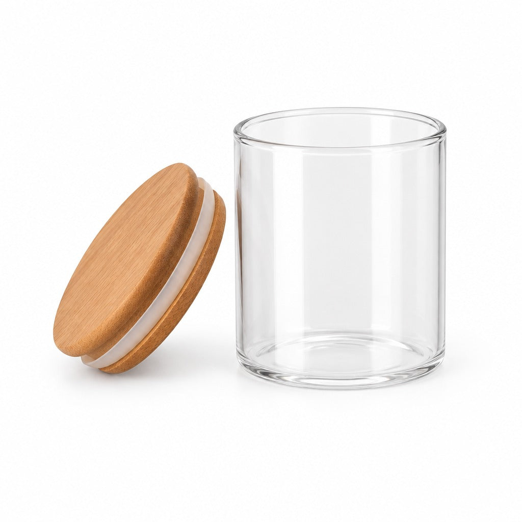 A clear cylindrical glass jar with a round bamboo lid resting beside it on a clean white background.