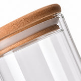 Close-up of a clear glass jar with a natural light brown wooden lid, showing the glass wall and wood grain against a white background.