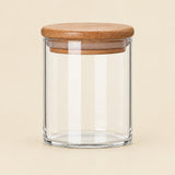 A clear glass jar with a round cork lid, shown on a solid light beige background.