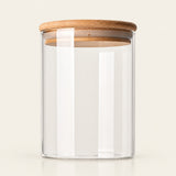 A clear glass storage jar with a light brown bamboo lid, shown on a clean, solid off-white background.