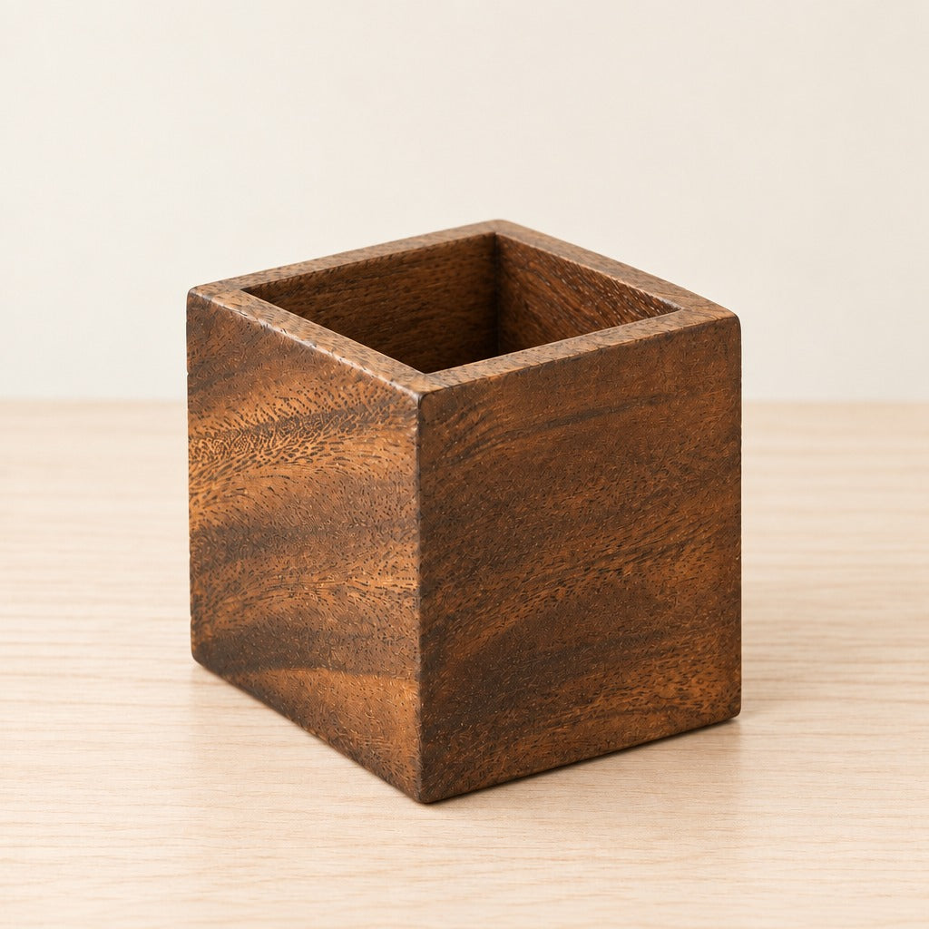 A square wooden holder with a deep open top, featuring a rich dark brown wood grain pattern, set on a light wood surface against a neutral cream background.