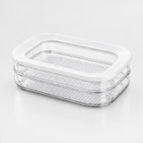 A clear plastic food storage container with a white lid, featuring two stacked perforated trays, shown on a clean white background.