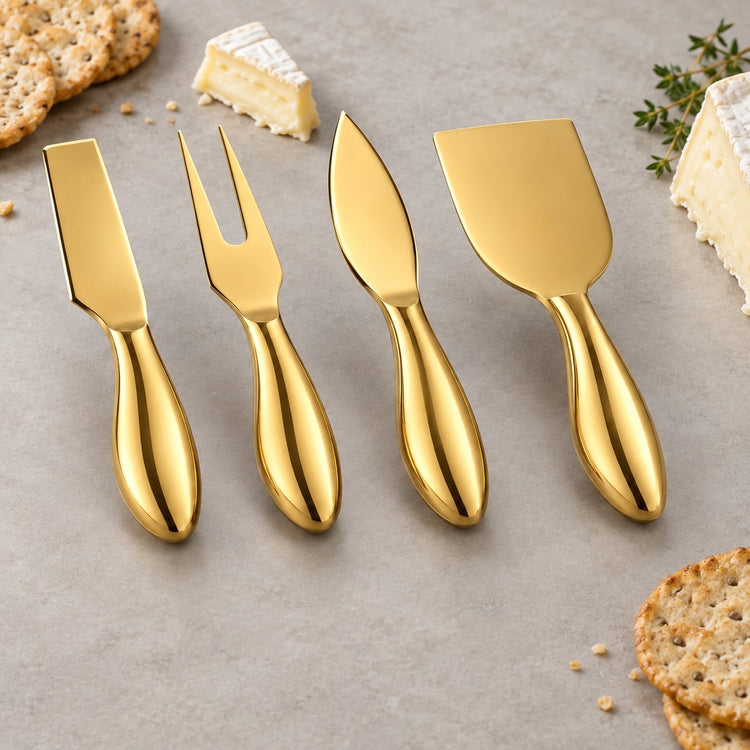 Four gold cheese knives and a fork arranged on a light gray surface with crackers and cheese wedges around them.