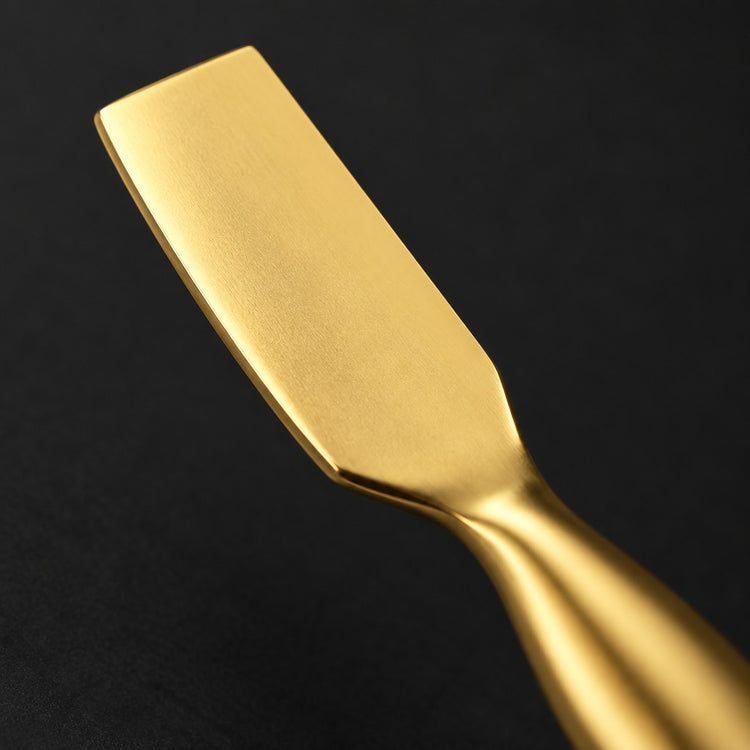 A close-up of a gold-colored metal spatula with a matte finish, set against a solid black background.