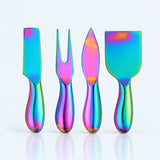 Four iridescent stainless steel serving utensils with colorful rainbow reflections, standing upright on a clean white background with a soft reflection below.