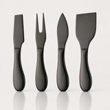 Four matte black cheese knives with different blade shapes, arranged in a row on a light gray reflective surface.