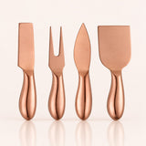 Four metallic cheese knives with polished copper-colored handles, arranged in a row against a clean off-white background with soft reflections below.
