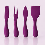 Four purple silicone cheese and wine utensils with ergonomic handles, arranged upright on a light pink reflective surface.