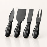Four black cheese knives with glossy handles, including a knife, a spatula, a straight knife, and a fork, arranged in a row on a light off-white background.