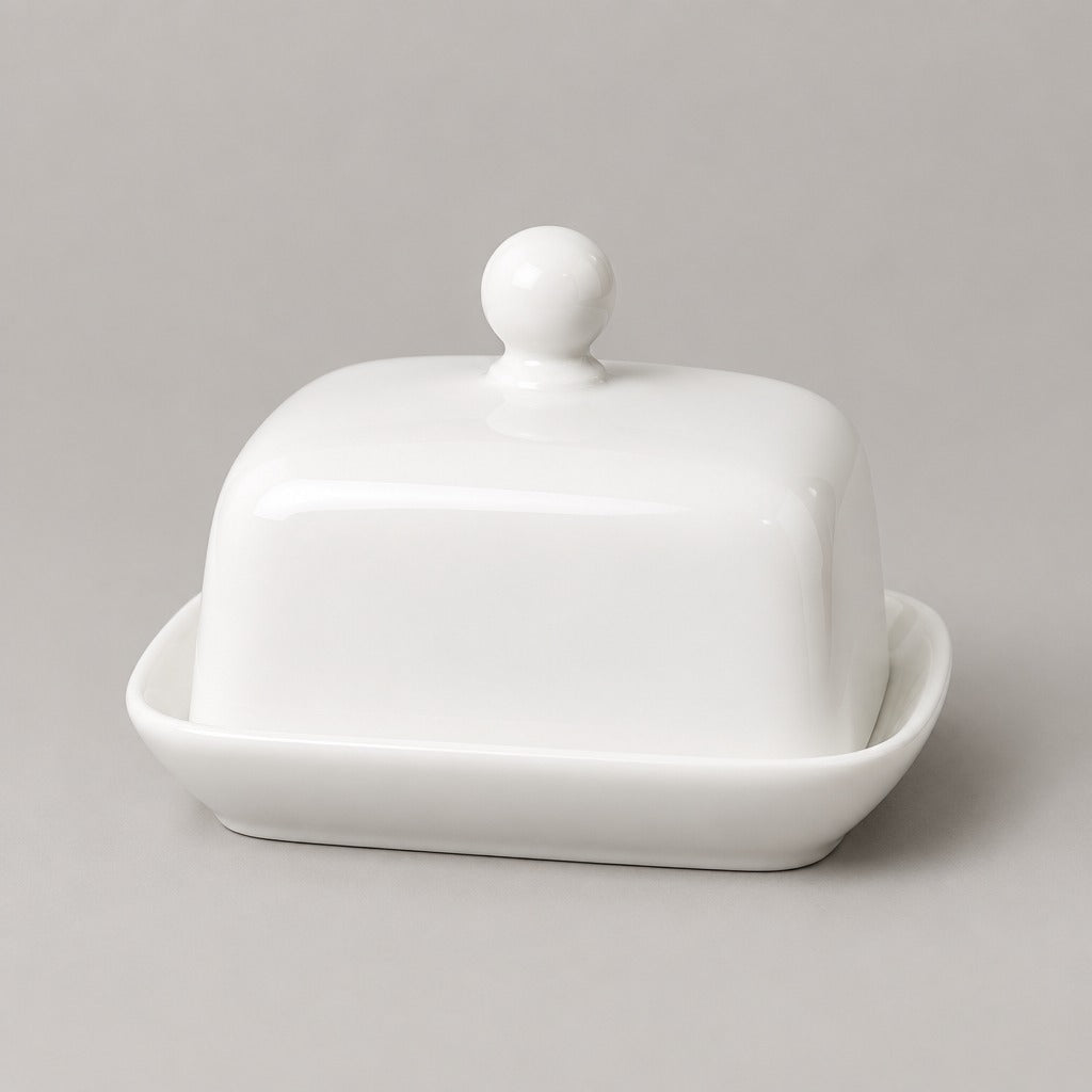 A white ceramic butter dish with a square lid featuring a rounded knob, set in a matching shallow base on a neutral gray background.