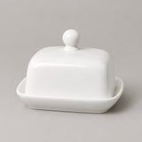 A white ceramic butter dish with a square lid featuring a rounded knob, set in a matching shallow base on a neutral gray background.