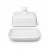 A white ceramic butter dish with its lid off, showing a rectangular tray with rounded corners and a matching rounded lid with a small knob on top, set against a plain white background.