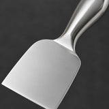 A close-up of a polished stainless steel spatula with a flat blade and curved handle, set against a dark gray background.