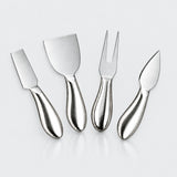 Four stainless steel cheese and carving utensils with ergonomic handles, arranged on a light gray reflective surface.