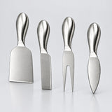 Four stainless steel cheese knives with ergonomic handles, arranged in a row on a light gray reflective surface.