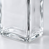 Close-up of a clear glass container corner with faceted edges and reflective surfaces on a light gray background.