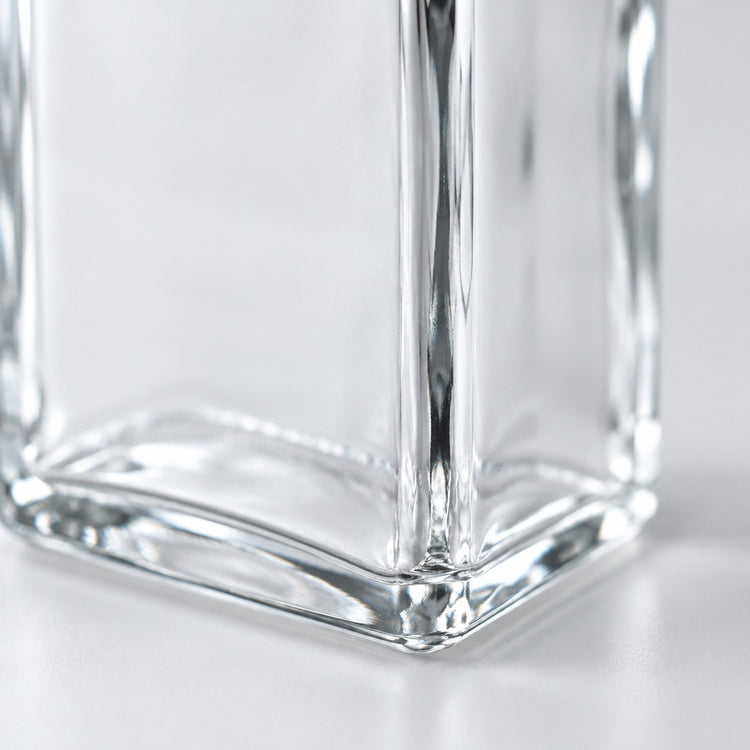 Close-up of a clear glass container corner with faceted edges and reflective surfaces on a light gray background.