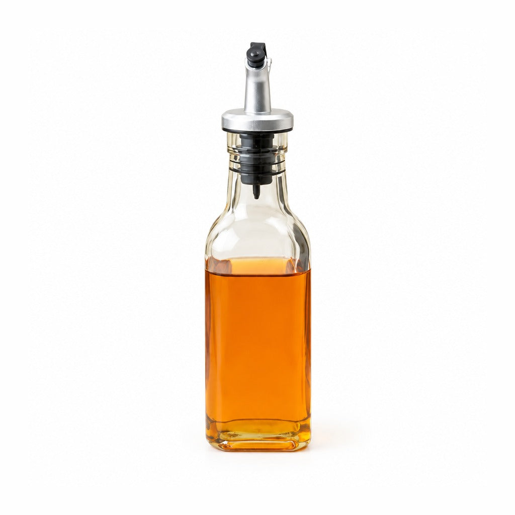 A clear glass bottle with a silver and black pour spout, filled with amber-colored liquid, shown on a plain white background.