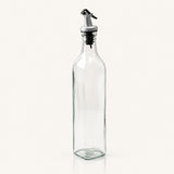 A tall, clear glass bottle with a silver and black metal pour spout, shown on a plain off-white background.