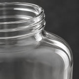 Close-up of a clear glass jar with a threaded neck, shown against a dark gray background.