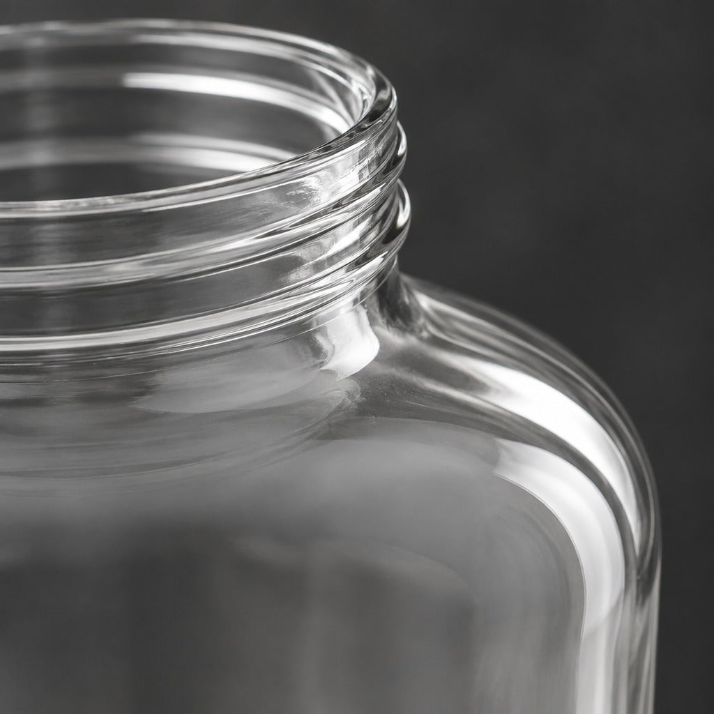 Close-up of a clear glass jar with a threaded neck, shown against a dark gray background.