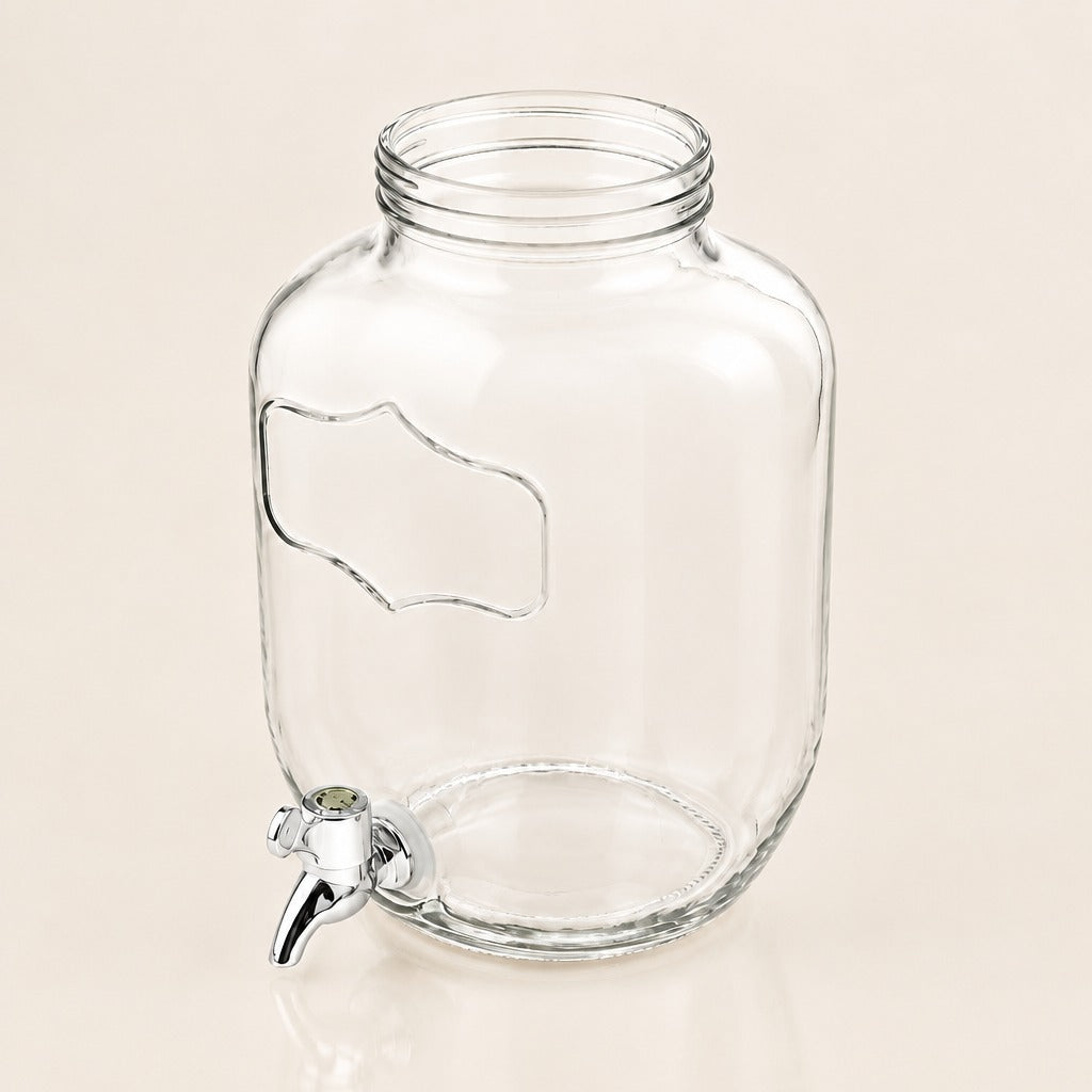 Clear glass beverage dispenser jar with a screw-top neck, side handle cutout, and a small metal spigot, shown on a plain warm beige background.