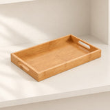 A rectangular bamboo serving tray with integrated cutout handles, resting on a white shelf in a minimalist, sunlit setting.