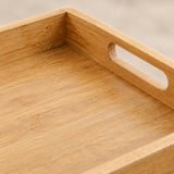 Close-up of a light natural wood tray with a handle cutout, showing the grain and warm tan color.