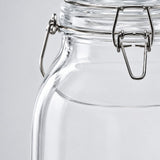 Close-up of a clear glass jar with a metal clamp lid on a light gray background.