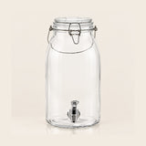 Clear glass beverage canister with a metal wire bail closure and a stainless steel spout, shown on a plain light beige background.