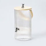 A ribbed clear glass beverage dispenser with a light wood lid, a small metal bear topper, and a side carry handle, shown on a light gray background.