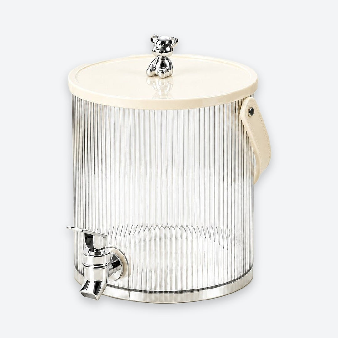 A ribbed clear glass beverage dispenser with a cream-colored lid, a small silver bear figurine on top, a side handle, and a chrome metal spout, shown on a light gray background.