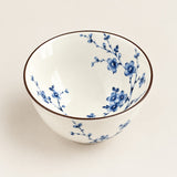 A white ceramic bowl decorated with blue floral patterns and a thin brown rim, shown from a top-down angle on a light beige background.