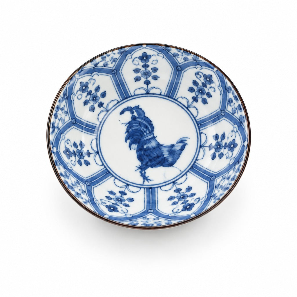 A round ceramic bowl with a blue and white hand-painted design, featuring a rooster in the center and floral motifs around the rim, set against a plain white background.