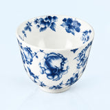 A white ceramic bowl decorated with a classic blue floral pattern, photographed against a light blue background.