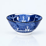 A blue and white patterned ceramic bowl with a hand-painted tree design, shown on a clean white background with a soft reflection underneath.