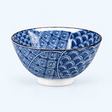 A ceramic bowl with a blue and white pattern, featuring geometric and scallop-like designs, set against a light blue background.