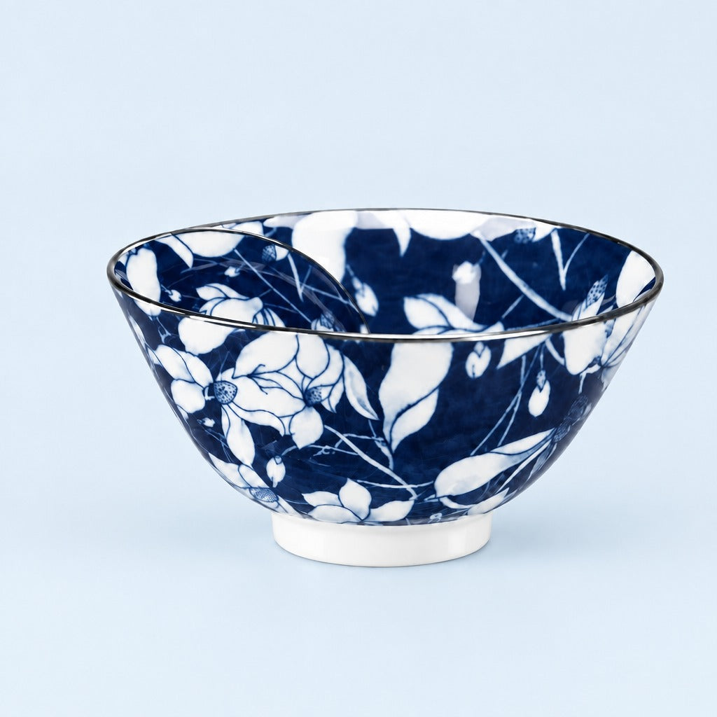 A ceramic bowl with a dark blue and white floral pattern, featuring a white footed base and a thin dark rim, set against a light blue background.