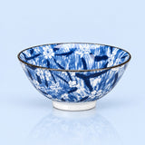 A blue and white patterned ceramic bowl with a dark rim, shown on a light blue reflective surface.