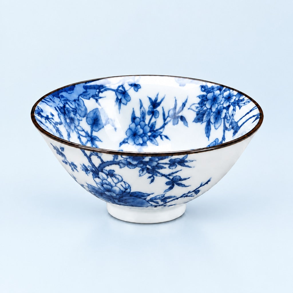 A white ceramic bowl decorated with a blue floral and bird pattern, featuring a thin dark rim and a small footed base, set against a light blue background.