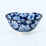 A ceramic bowl with a blue and white floral pattern, featuring a white footed base and a thin black rim, photographed on a clean white background.