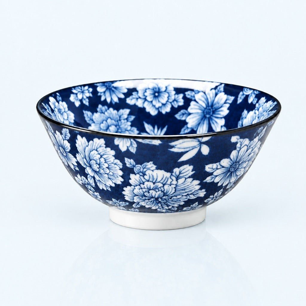 A ceramic bowl with a blue and white floral pattern, featuring a white footed base and a thin black rim, photographed on a clean white background.