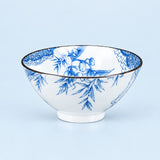 A white ceramic bowl decorated with a blue floral and botanical pattern, featuring a thin dark rim, set against a solid light blue background.
