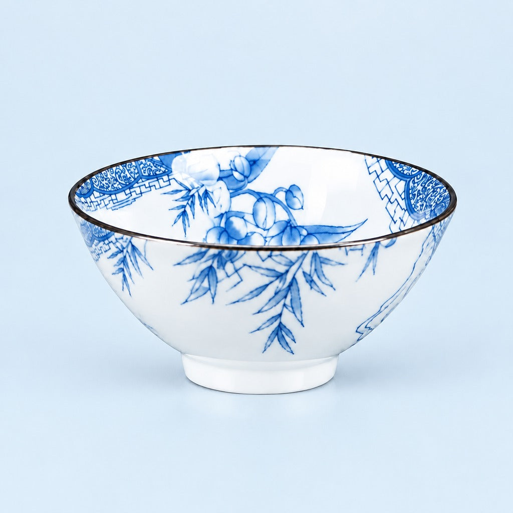 A white ceramic bowl decorated with a blue floral and botanical pattern, featuring a thin dark rim, set against a solid light blue background.