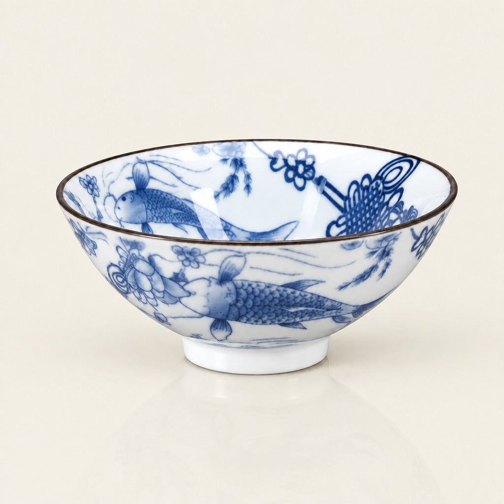 A white ceramic bowl decorated with blue hand-painted fish and floral motifs, featuring a thin dark rim, set against a plain light beige background.