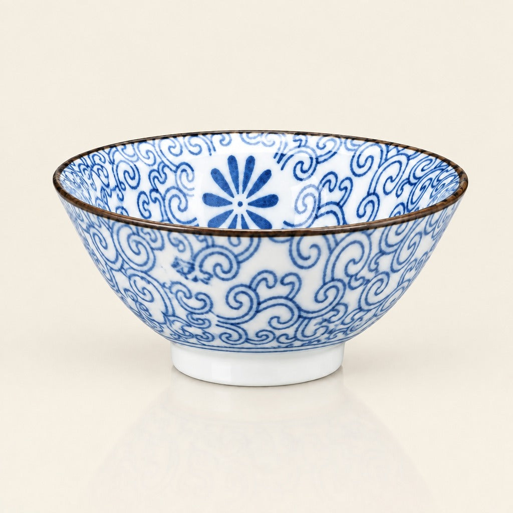 A white ceramic bowl decorated with blue hand-painted floral and scroll patterns, featuring a thin dark rim and a small white footed base, set against a plain off-white background.